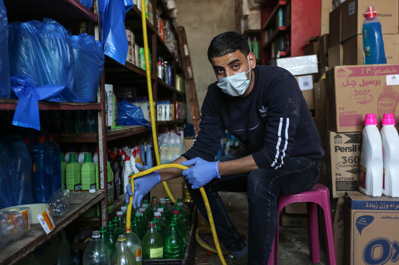 A young man wearing a face mask fills a plastic bottle from a yellow hose