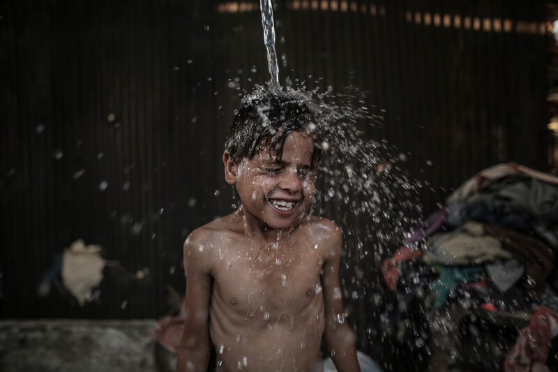 A boy smiles as water is poured over his head