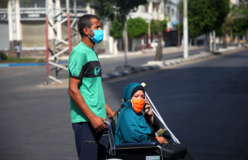 Man rolls woman on wheelchair, both wearing protective masks 
