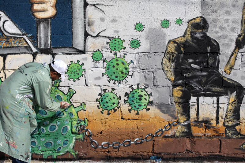 Man paints wall with images representing the virus and prisoners