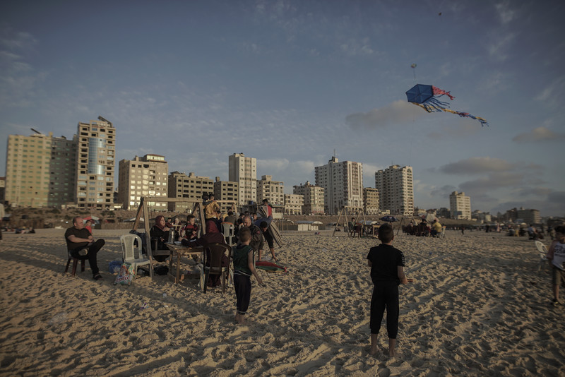 Children play with kites and adults watch as sun goes down over Gaza beach