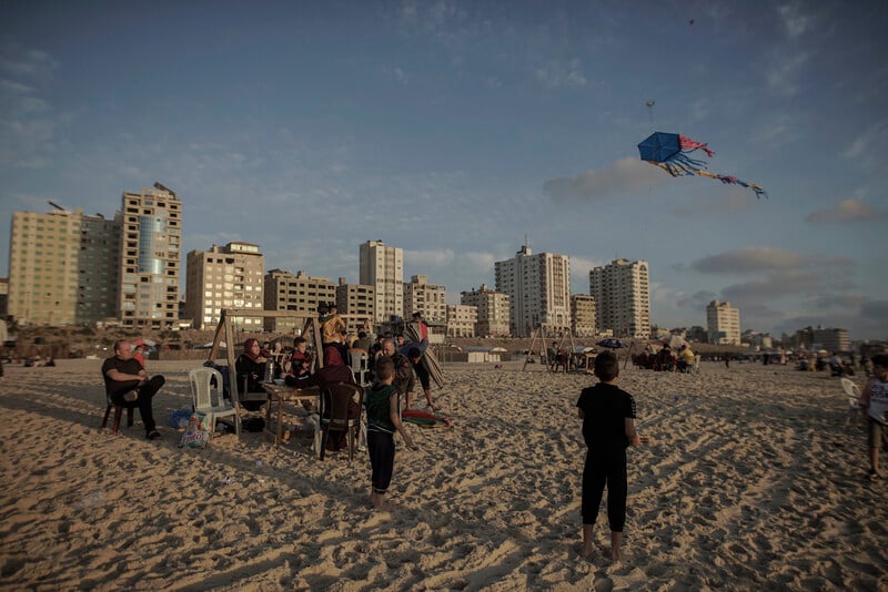 Children play with kites and adults watch as sun goes down over Gaza beach