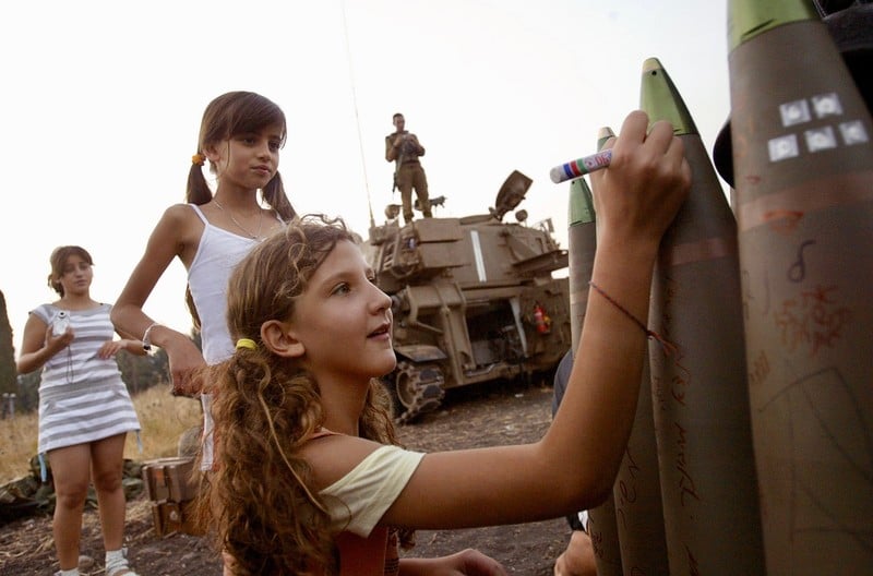 Smiling girl writes on munition as others look on