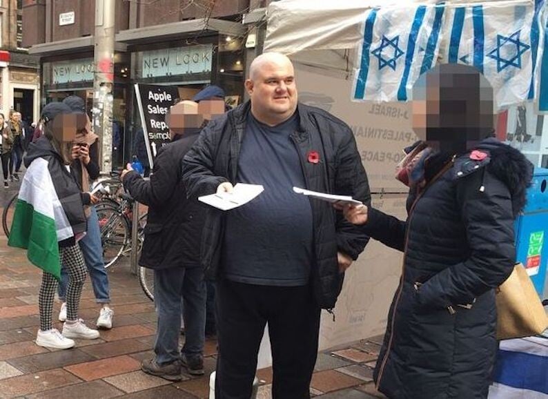 A man hands out leaflets at a stall with Israeli flags