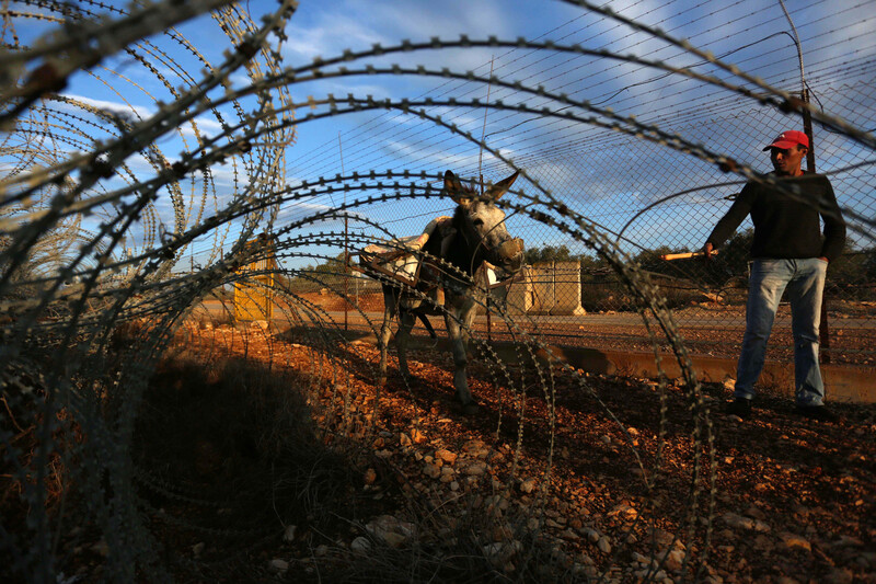 A man and his donkey is seen through barbed wire