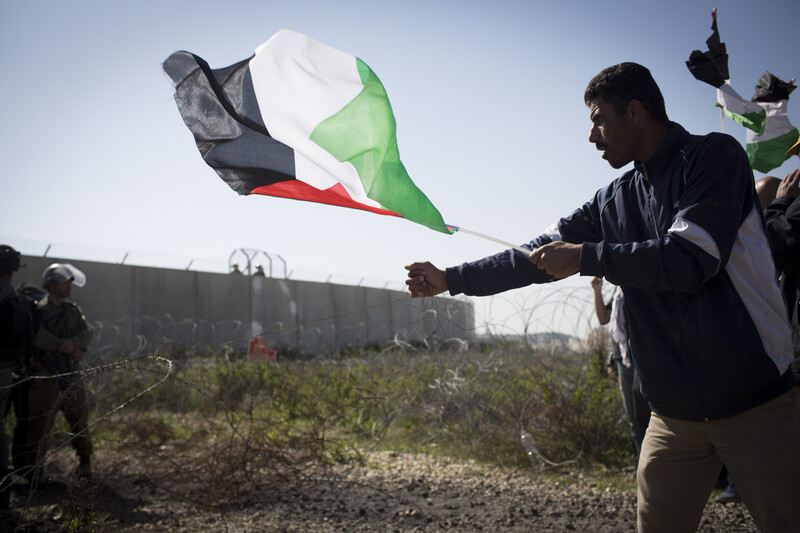 Man holding Palestine flag grabs barbed wire fence near Israeli soldiers