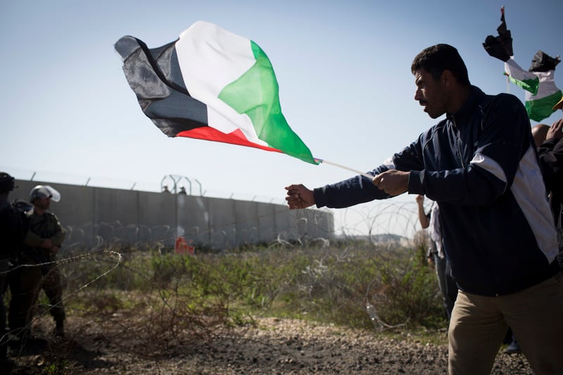 Man holding Palestine flag grabs barbed wire fence near Israeli soldiers