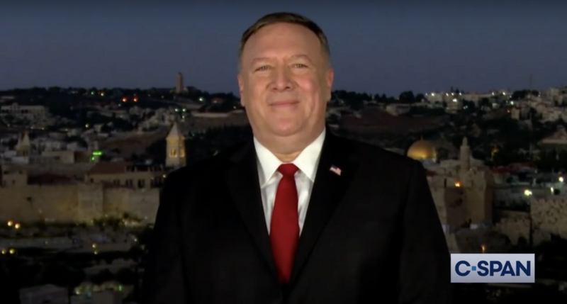 Man speaks to camera with evening cityscape behind him