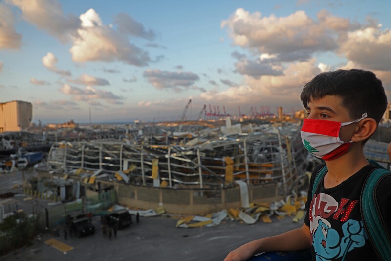 Boy stands in front of landscape of destroyed buildings