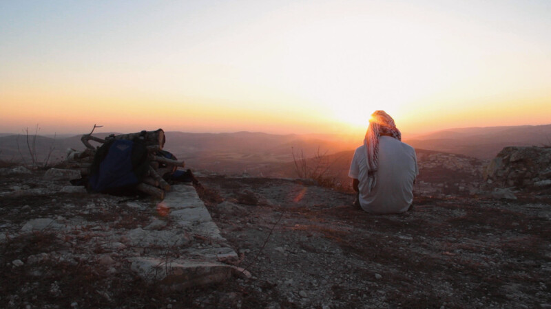 Man sits on rocky outcrop with back to camera 