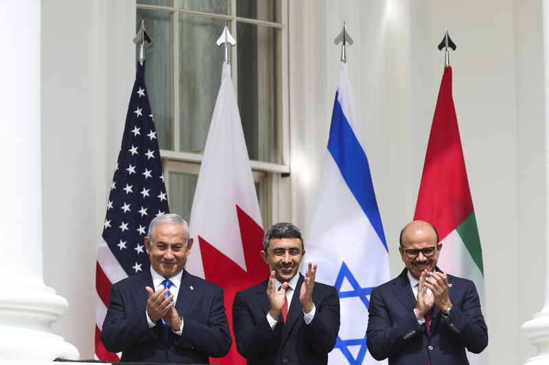 Three men clap in front of large flags 