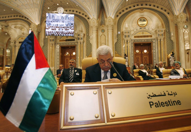Mahmoud Abbas sits in a gold-themed room behind a sign with Palestine written on it