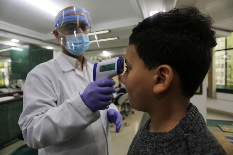 A doctor wearing a face mask is taking a boy's temperature