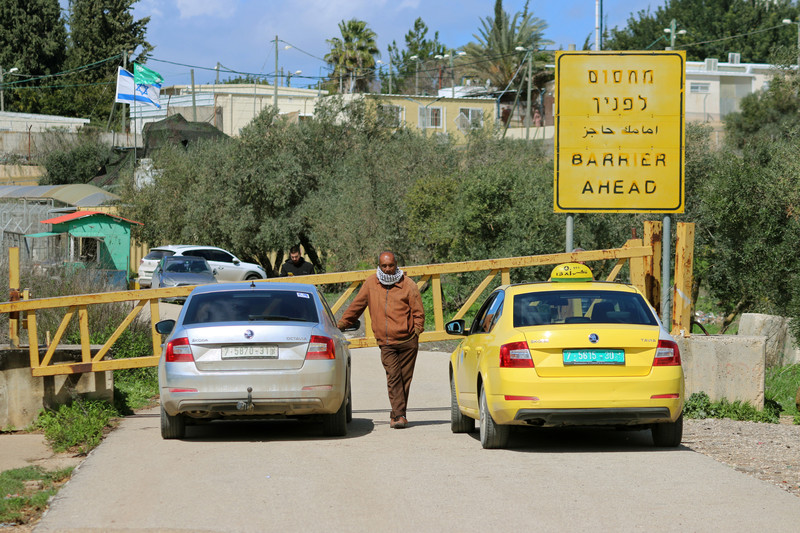 Two cars are stopped at a metal barrier with a sign in Hebrew, Arabic and English