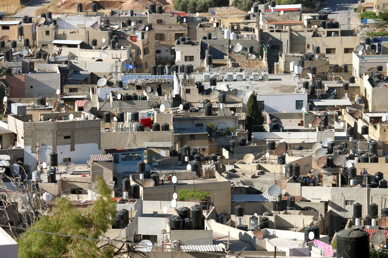 A crowded bunch of rooftops topped with black water tanks and white satellite dishes jostle for space