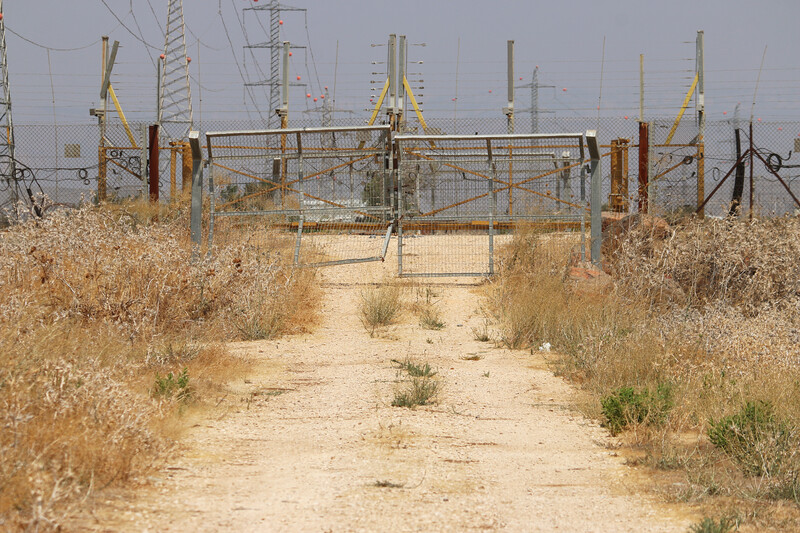 A metal gate and fence cuts across a dirt road