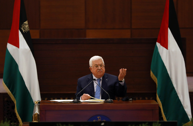 Mahmoud Abbas gestures while seated between two Palestinian flags