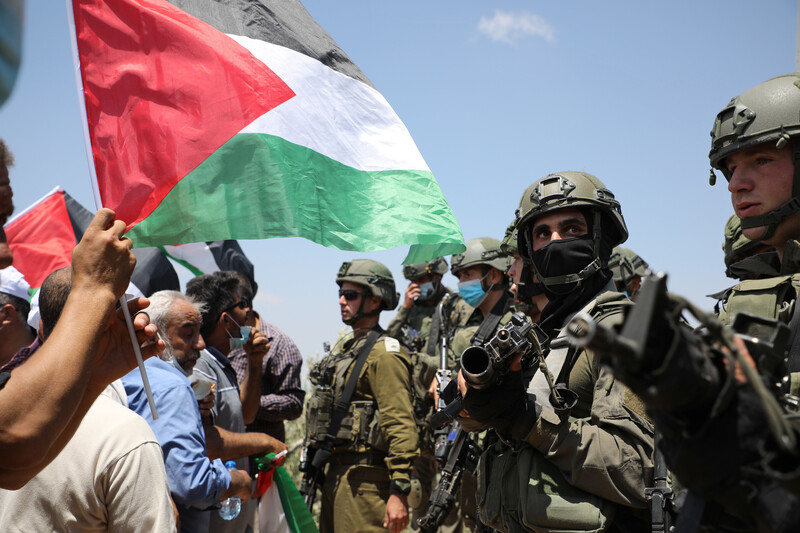 A Palestine flag waves in front of Israeli soldiers