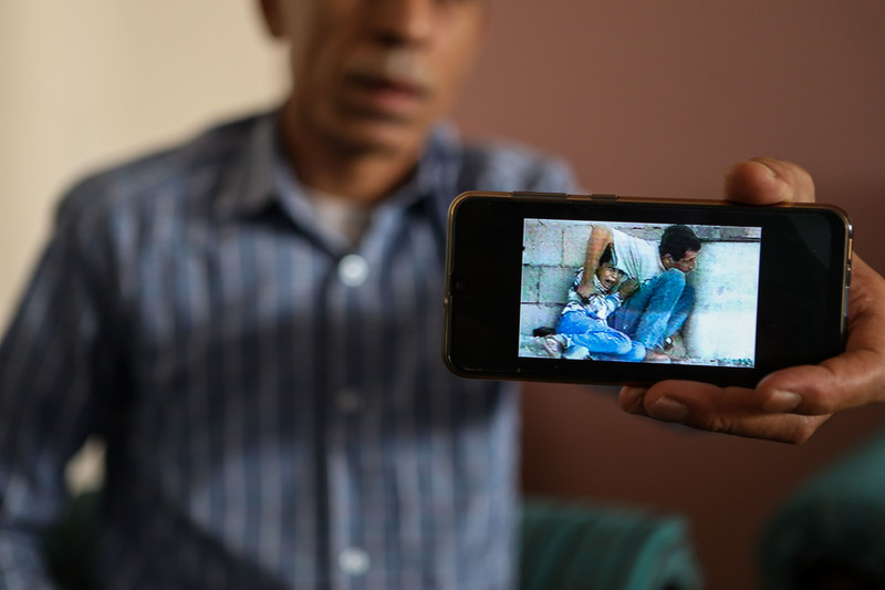 A man holds out a mobile phone showing a still from grainy video footage