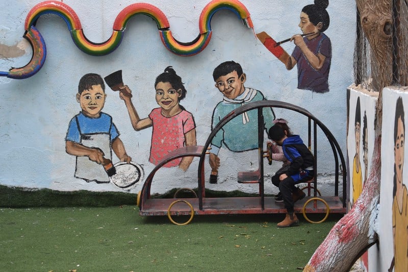 Children play outside in front of a brightly painted wall