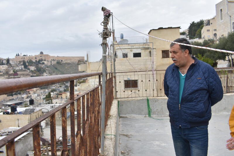 A man looks out from a balcony with a rusty fence