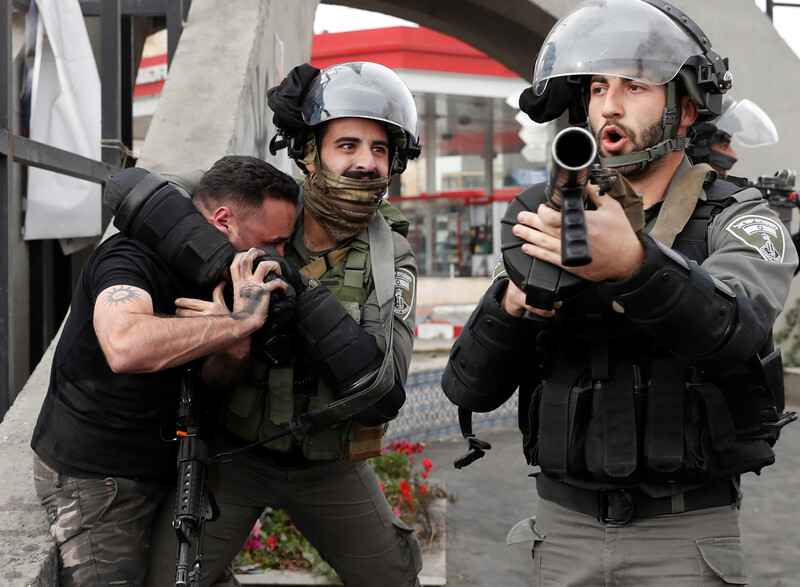 An Israeli police officer puts a Palestinian in a choke hold while another officer points a gun