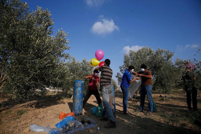 A group of men stand in a field of trees with a number of colorful balloons