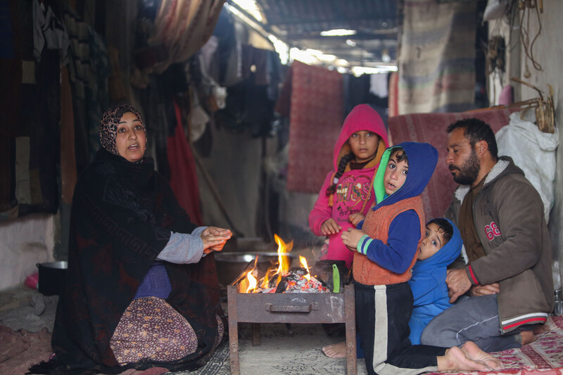 Two adults and two children warm their hands against a wood fire