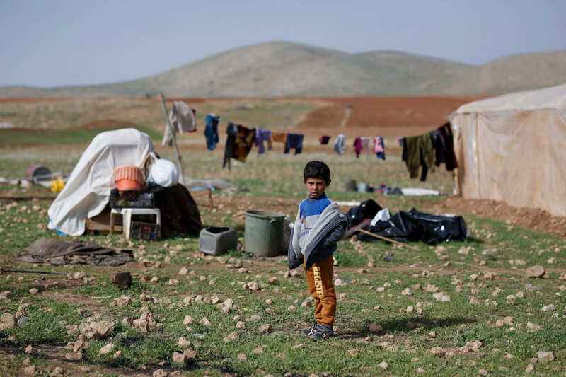Boy stands near clothes line and scattered structures