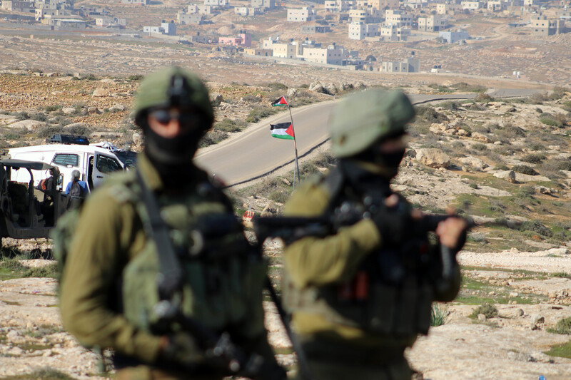 Two soldiers take position, Palestinian flag in the background 