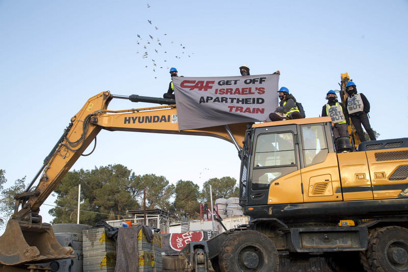 People on top of construction equipment hold banner