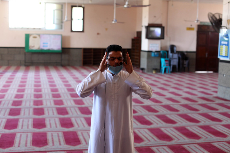 A man raises his hands to his head in prayer in an otherwise empty room
