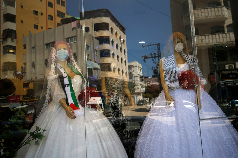 Two mannequins in wedding dresses and face masks are seen through through a shop window