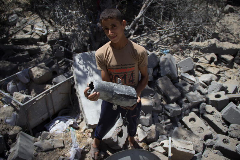 Boy holding metal object stands amid rubble
