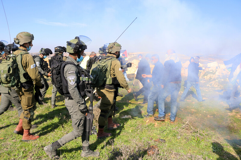 Uniformed soldiers face off against unarmed protestors hidden by a cloud of tear gas