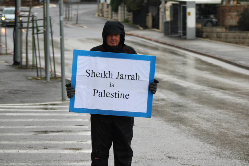 A person wearing a winter coat holds a sign in the street 