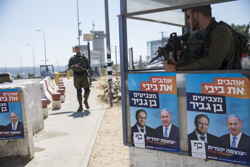 A soldier stands at a concrete checkpoint plastered with posters