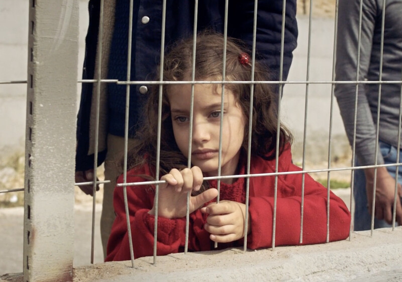 A girl stands behind a metal grill