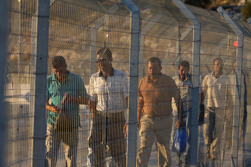 A group of men walk behind a metal fence