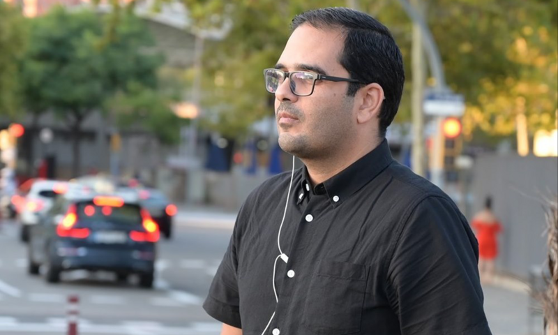 Un hombre con una camisa abotonada y un auricular se encuentra en la calle. 