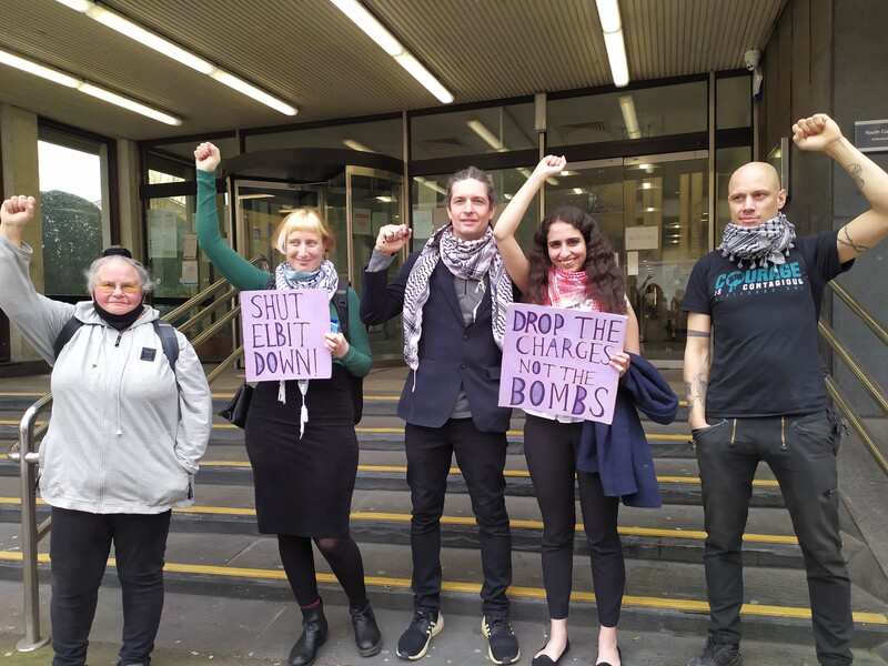 Five people raising fists and holding two signs