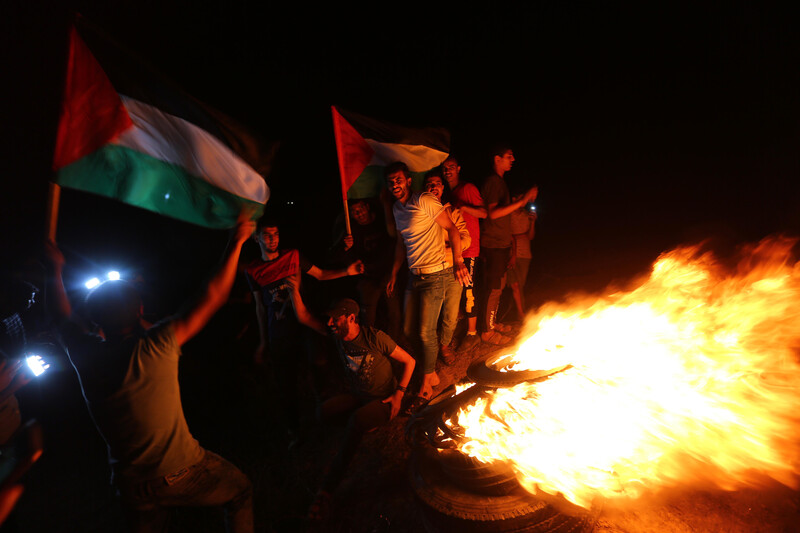 Young men smile while holding flags and standing next to a fire at night