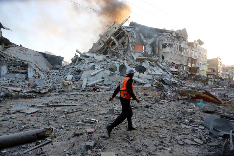 A man in an orange vest walks past the rubble of a building