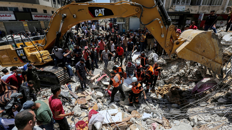 A crowd of people stand under an excavation machine on an urban street