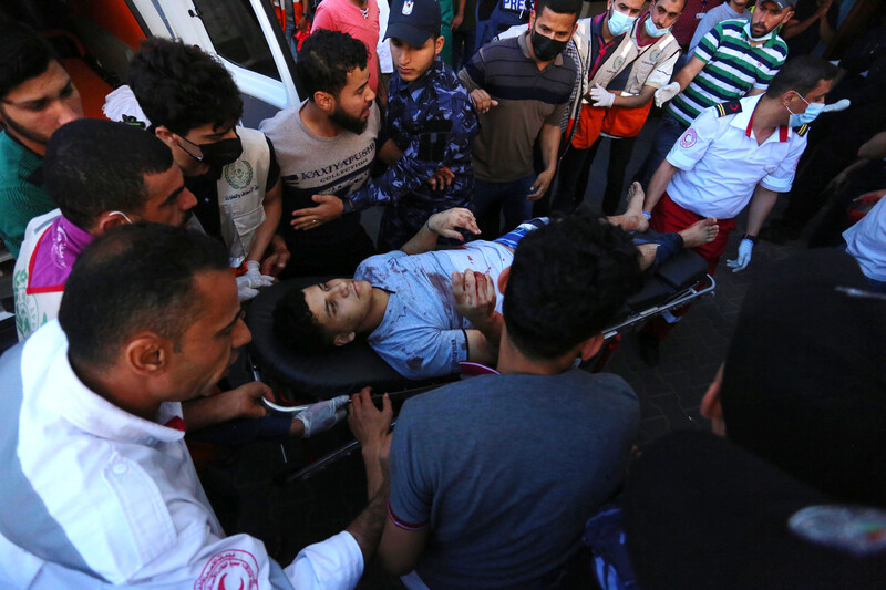 A young man with bloodied clothes lies on a stretcher amid crowd next to ambulance