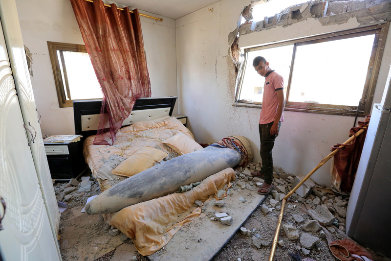 Youth looks at missile that landed on bed in debris-strewn room