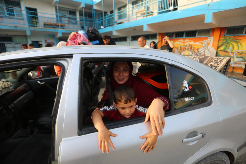 Woman and boy smile while looking out of car in front of UN school