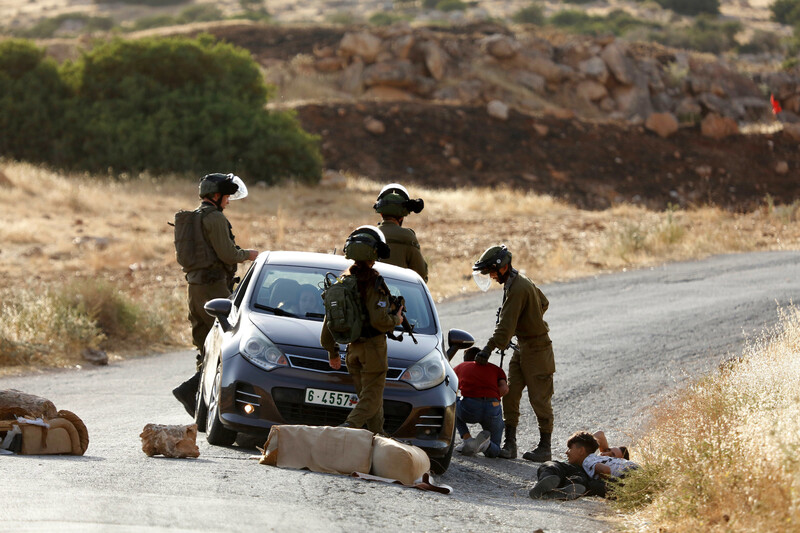 Four soldiers detain youths lying on the street next to a car