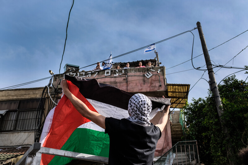 A man holds a flag up as people on top of a building look down