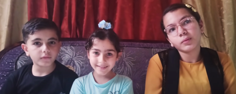 A boy and two girls are seated next to each other on a couch 